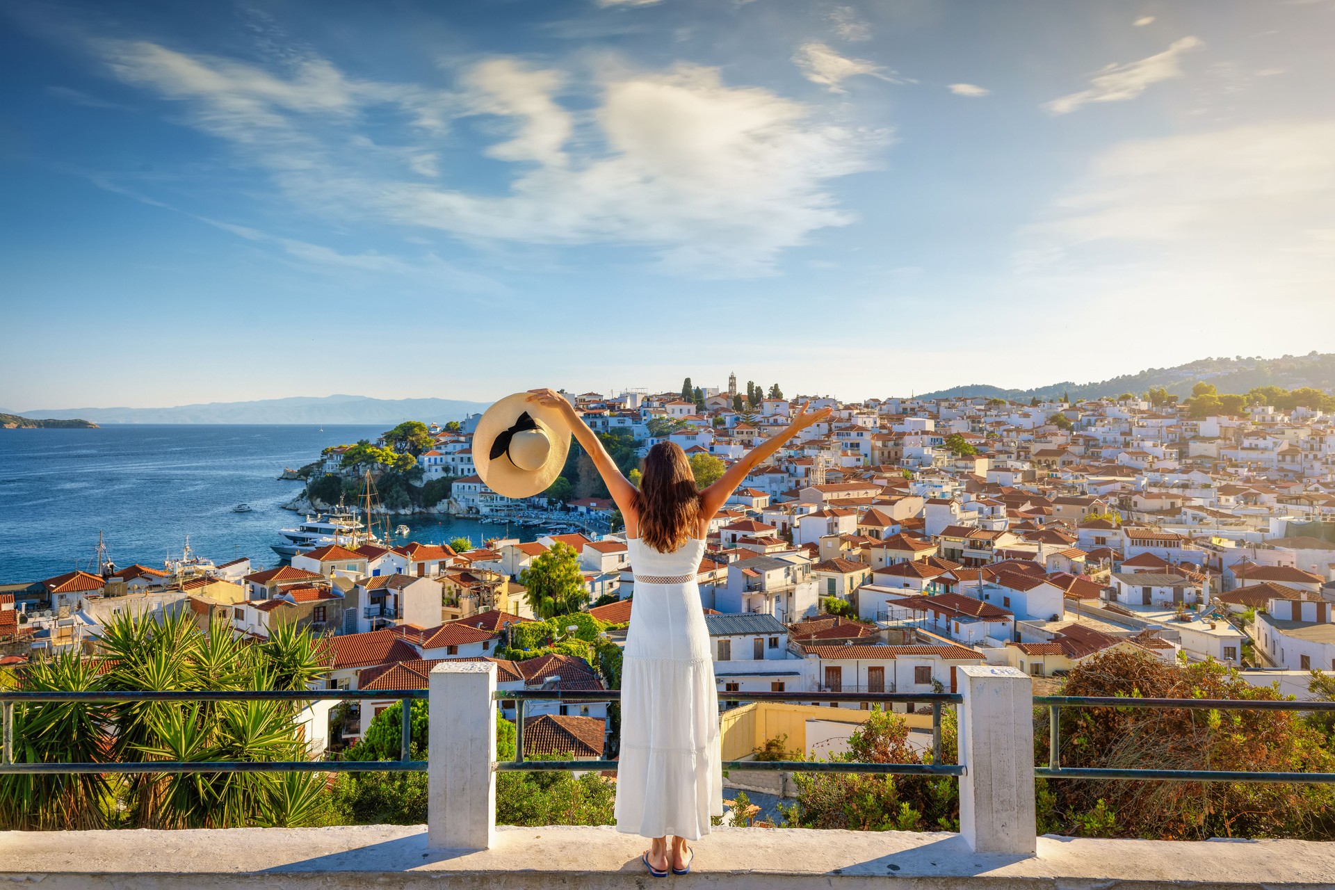 A tourist woman enjoys the sunset view of the town of Skiathos island A tourist woman enjoys the sunset view of the town of Skiathos island